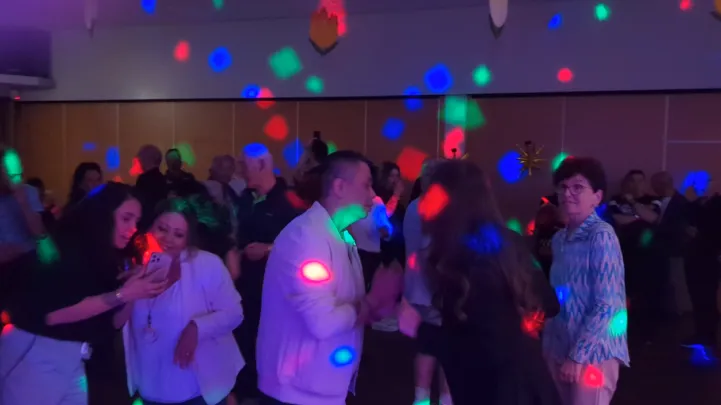 Gasten dansen en proosten op een volle dansvloer onder paarse en blauwe discoverlichting tijdens een evenement in Geleen