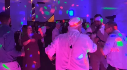 Gasten op de dansvloer, inclusief een man met een witte hoed en bretels, dansen onder kleurrijke discoverlichting op een bruiloft in Limburg.