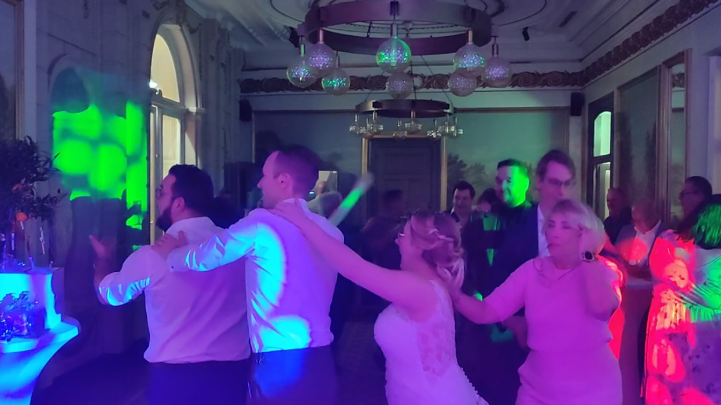 Een energieke polonaise op de dansvloer van Kasteel Vaeshartelt tijdens een bruiloft, verlicht door dynamische groene en roze DJ-verlichting.